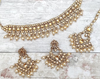 Pode incluir: Um conjunto de colar e brincos de ouro com detalhes em âmbar e pérolas. O colar é de estilo choker com uma corrente delicada e um pingente com design floral. Os brincos são de estilo gota com um design floral semelhante.