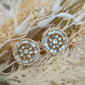 Op de afbeelding: Een paar ronde, witte en gouden oorbellen met een bloemmotief. De oorbellen zijn gemaakt van parelmoer en hebben een parelrand.