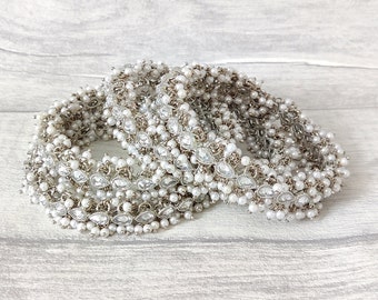 May include: A set of four silver and white beaded bracelets with decorative accents. The bracelets are stacked on top of each other.