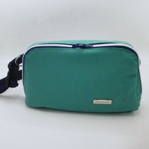 May include: A teal blue zippered pouch with a white zipper and a white and blue trim. The pouch has a black strap and a silver label that says "handmade".