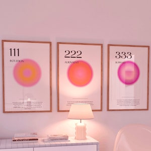 May include: Three framed prints with pink and orange gradient circles and the numbers 111, 222, and 333 with the words "Intuition", "Alignment", and "Support" below each number. The prints are hanging on a white wall above a white dresser with three drawers and a white chair.