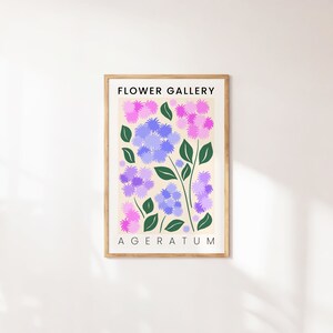 May include: A framed print with the title "FLOWER GALLERY" and the name of the flower "AGERATUM" in black text. The print features a stylized illustration of purple and pink flowers with green leaves on a cream background.