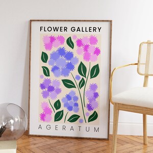 May include: A framed print with a floral design featuring purple and pink flowers with green leaves. The print has the text "FLOWER GALLERY" and "AGERATUM" in black.