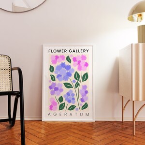 May include: A framed print with a cream background featuring a stylized illustration of purple and pink flowers with green leaves. The text "FLOWER GALLERY" and "AGERATUM" is printed in black at the top and bottom of the print.