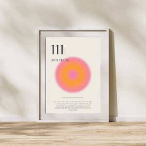 May include: A white framed poster with the number 111 and the word "INTUITION" in black text. A pink and orange circle with a smaller orange circle in the center is in the middle of the poster. The text below the circle reads: "You are here to work wonders on other people. Discover your inner power, you already possess all the tools you require to manifest the things you desire. Embrace your responsibility as a spiritual guide, and you'll strengthen people's faith. Show what is possible when you use your own unique strengths."