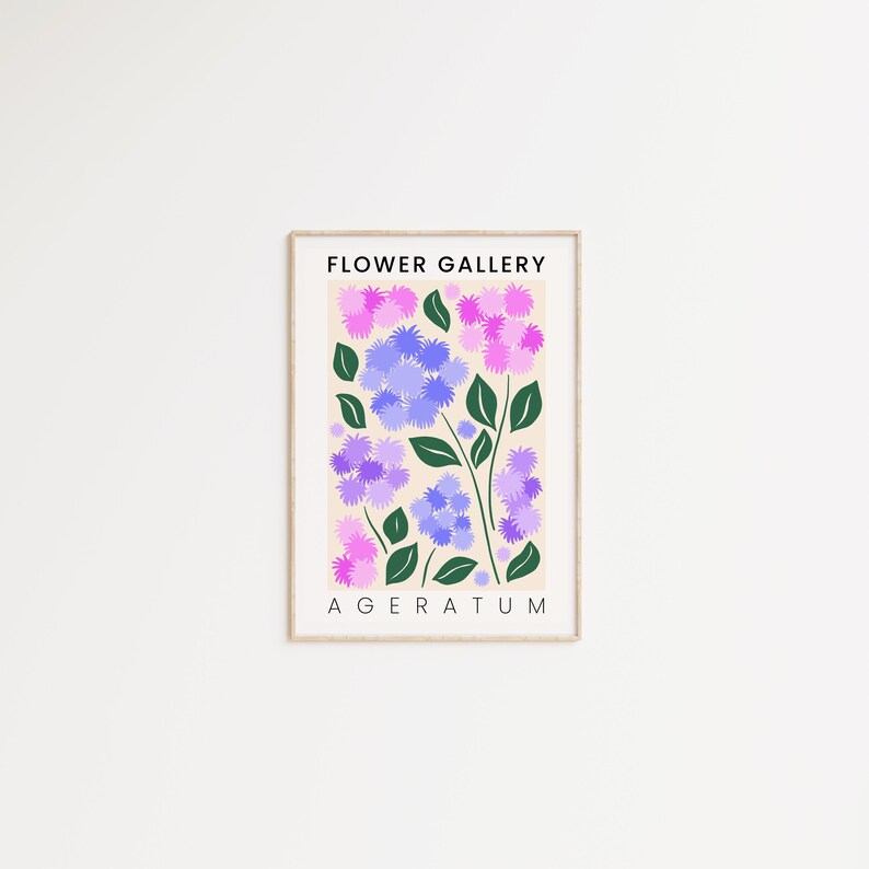 May include: A framed print with a light beige background featuring a stylized illustration of purple and pink flowers with green leaves. The text "FLOWER GALLERY" and "AGERATUM" is printed in black at the top and bottom of the print.