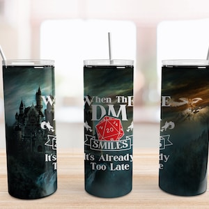 May include: Three stainless steel tumblers with a dark fantasy theme. The center tumbler features a red twenty-sided die with the text "When the DM Smiles It's Already Too Late". The left tumbler features a dark castle with a dragon flying overhead. The right tumbler features a dragon flying over a mountain range.