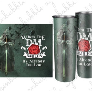 May include: Two green and black stainless steel tumblers with a graphic of a hooded figure holding a sword. The tumblers feature the text "When The DM Smiles It's Already Too Late" and a red 20-sided die.