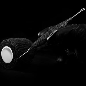 May include: A black roll of athletic tape with a white center and a black, metal needle with a loop at the end.