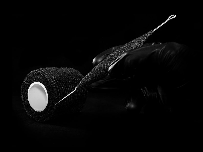 May include: A black roll of athletic tape with a white center and a black, metal needle with a loop at the end.