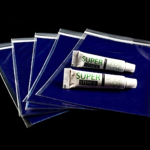 Puede incluir: Cinco bolsas de plástico transparentes con cierre de cremallera, apiladas unas sobre otras. Dos tubos blancos de adhesivo Super Stencil están encima de las bolsas.