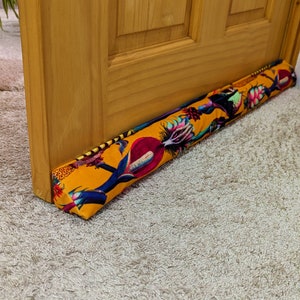 以下が含まれることがあります： カラフルな花柄の黄色いドアストッパー。ドアストッパーは木製のドアの下部に置かれています