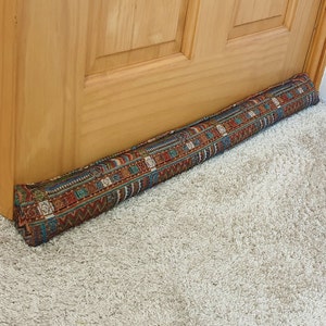 May include: A brown doorstop with a colourful patterned fabric cover. The doorstop is placed on a light beige carpet.