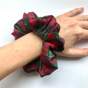 Pode incluir: Scrunchie xadrez vermelho, verde e preto com detalhes em fio dourado.