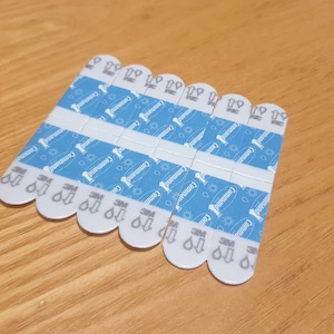 Puede incluir: Un paquete de 12 tiras adhesivas blancas de la marca Command con un patrón azul. Las tiras están diseñadas para colgar objetos ligeros en las paredes.