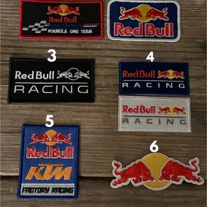 May include: Six different Red Bull Racing patches. The patches are all embroidered and feature the Red Bull logo, the words "Red Bull Racing", and the number "1" on the first patch. The patches are all different colors and sizes.