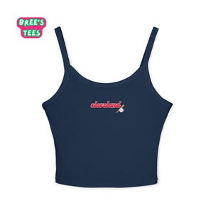May include: A navy blue crop top with spaghetti straps. The word "cleveland" is embroidered in red script, with a baseball and bat graphic. The top has the "Bree's Tees" logo in the upper left corner.