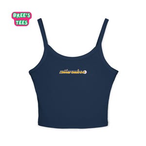 Op de afbeelding: Marineblauwe crop top met dunne bandjes. Het woord "milwaukee" is geborduurd in een gouden scriptlettertype, met een honkbalafbeelding. De top heeft de tekst "Bree's Tees" in een roze en groene bubbel. Een casual, sportieve stijl.