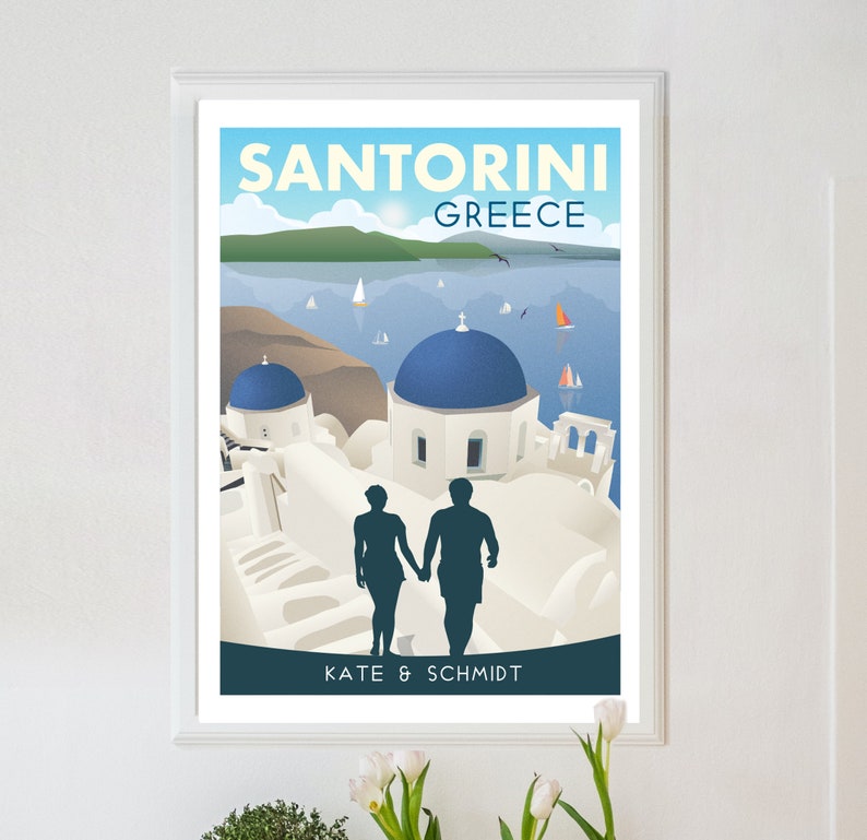 May include: A travel poster featuring a couple silhouetted in front of a white building with blue domes in Santorini, Greece. The poster has the text "Santorini Greece" and "Kate & Schmidt" at the bottom.