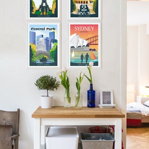 May include: Four framed travel posters with a vintage aesthetic. The posters feature illustrations of the Eiffel Tower in Paris, the Colosseum in Rome, Central Park in New York City, and the Sydney Opera House in Sydney, Australia. Each poster has the city name and location at the top, and the text "KATE & SCHMIDT" at the bottom.