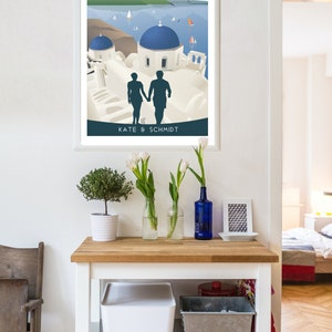 May include: A white framed poster with a colorful illustration of Santorini, Greece. The poster features a couple walking hand-in-hand in front of white buildings with blue domes. The text "Santorini Greece" is at the top of the poster and "Kate & Schmidt" is at the bottom.