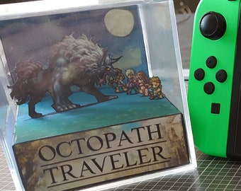May include: A green Nintendo Switch console with a black controller and a clear acrylic box containing a 3D papercraft model of a monster and characters from the video game Octopath Traveler. The console screen displays the game Octopath Traveler and other games. The text "THE PERFECT GIFT!" is written on the table below the console.
