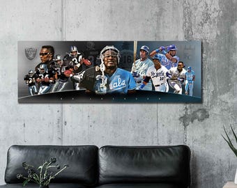 May include: A rectangular wall art print featuring a collage of football and baseball players in action. The print includes the Raiders logo and the text "Royals". The color palette includes black, silver, and blue.