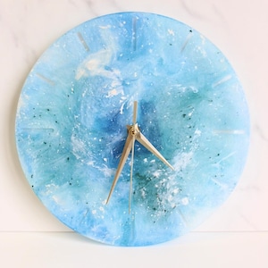 May include: A blue and green resin clock with gold hands. The clock face has a marbled effect with white and blue swirls.