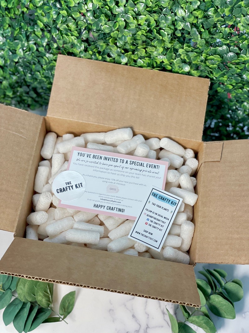 Pode incluir: Uma caixa de cart&atilde;o castanho cheia de amendoins de embalagem brancos. Um cart&atilde;o rosa e branco com o texto "Voc&ecirc; foi convidado para um evento especial!" e um autocolante com o texto "The Crafty Kit" s&atilde;o vis&iacute;veis.