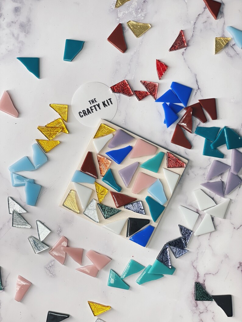 May include: A close-up of a mosaic tile kit with a variety of colors and shapes. The kit includes a small square tile with a mosaic design, as well as a variety of loose tiles in different colors and shapes. The kit is labeled "The Crafty Kit".