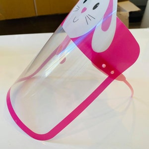 May include: Pink plastic face shield with a clear visor and a white bunny design. The bunny has black eyes and a pink nose.