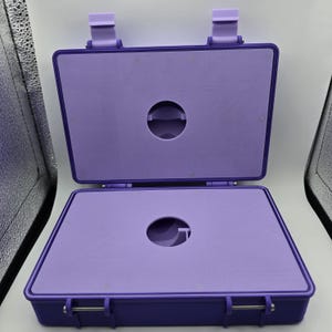 Pu&ograve; includere: Valigetta rettangolare viola aperta con interno abbinato. La valigetta ha un coperchio incernierato e un ritaglio circolare al centro della base e del coperchio. La valigetta &egrave; fissata con due chiusure e due chiusure superiori.