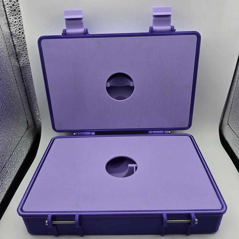 Pu&ograve; includere: Valigetta rettangolare viola aperta con interno abbinato. La valigetta ha un coperchio incernierato e un ritaglio circolare al centro della base e del coperchio. La valigetta &egrave; fissata con due chiusure e due chiusure superiori.