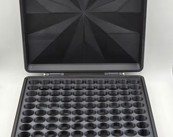May include: A black, open case with a geometric design on the lid. The interior features numerous circular compartments, suggesting organization. The case is designed to hold small items, possibly for storage or display.