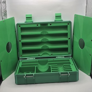 Pu&ograve; includere: Cassetta degli attrezzi in plastica verde aperta con pi&ugrave; scomparti e una maniglia. La cassetta degli attrezzi &egrave; aperta, rivelando varie sezioni di stoccaggio e una serie di ripiani. Due pannelli verdi sono su entrambi i lati.