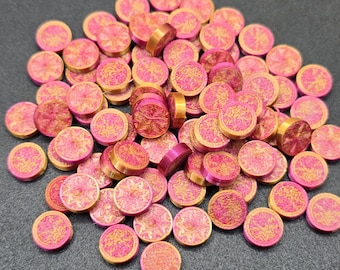May include: A pile of pink and gold round chips with a decorative design. The chips are about 1 inch in diameter.
