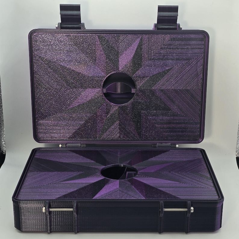 Pu&ograve; includere: Valigetta viola aperta con un design geometrico a forma di stella sulla parte superiore e inferiore. La valigetta ha una maniglia e due chiusure. L'interno ha un ritaglio circolare. La valigetta &egrave; realizzata in un materiale strutturato.