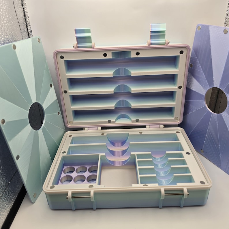 Pu&ograve; includere: Valigetta portaoggetti aperta con pi&ugrave; scomparti in tonalit&agrave; pastello. La valigetta &egrave; azzurra con un bordo rosa e un interno bianco, che rivela ripiani e scomparti. Due pannelli geometrici coordinati sono su entrambi i lati.