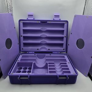 Pu&ograve; includere: Una cassetta degli attrezzi viola, aperta, con pi&ugrave; scomparti e un coperchio incernierato. L'interno presenta varie fessure e supporti per organizzare utensili o forniture. Il coperchio &egrave; staccato, rivelando l'interno. La cassetta &egrave; realizzata in materiale resistente.