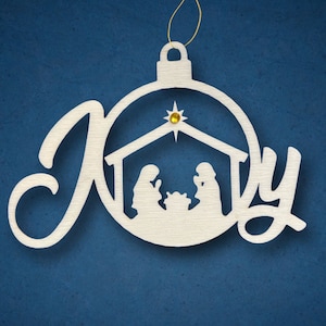 Pode incluir: Ornamento de Natal de madeira branca em forma de círculo com a palavra "Joy" escrita em letra cursiva. O centro do ornamento apresenta uma cena de natividade com uma estrela sobre o presépio.