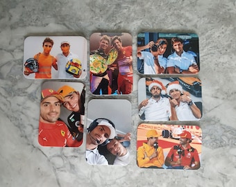 May include: A collection of rectangular coasters with images of Formula 1 drivers. The coasters show drivers in various settings, including portraits and celebrations. The images are printed on a light-coloured surface.