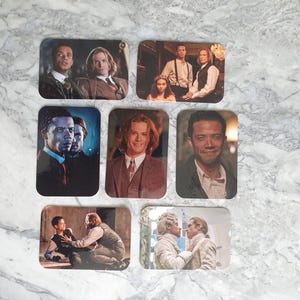 May include: Six rectangular coasters, each displaying a different image of characters from a television show. The coasters showcase various scenes and portraits, with a glossy finish. The images are set against a marble background.