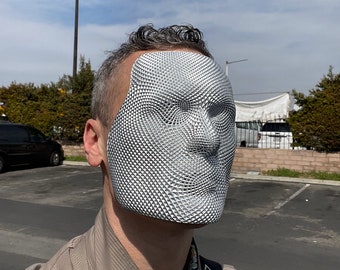 May include: A person wearing a silver 3D printed face mask with a geometric pattern. The mask covers the entire face, including the eyes, nose, and mouth.