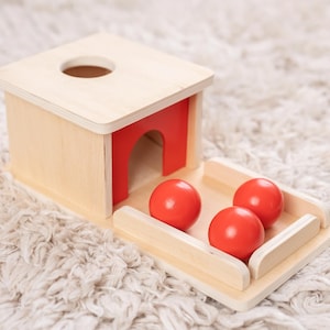 May include: Wooden toy box with a red opening and three red balls. The box is open and the balls are visible.