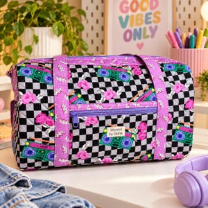 Puede incluir: Una bolsa de viaje acolchada con un patrón de tablero de ajedrez en blanco y negro, rosas rosas, radiocasetes verdes y rayos. La bolsa tiene correas moradas y un bolsillo frontal con cremallera y una etiqueta Stitched by DARIA.