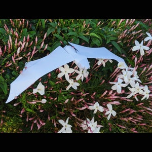 May include: A white paper airplane flying over a bush of white jasmine flowers with pink buds.