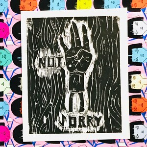 May include: Black and white linocut print of a hand with four fingers raised, with the words "NOT SORRY" printed below the hand.