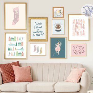Könnte beinhalten: Eine Galeriewand mit verschiedenen weihnachtlichen Drucken, darunter ein Strumpf, eine Schneekugel, eine Fee und Zuckerstangen. Die Drucke sind in Gold gerahmt und an einer weißen Wand angeordnet. Die Wand befindet sich über einem weißen Sofa mit zwei rosa Kissen.