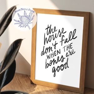 May include: A framed print with a black and white handwritten quote that reads "These houses don't fall when the bones are good".