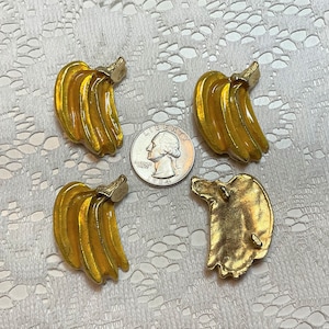 May include: Four yellow banana-shaped metal buttons with a shiny finish. The buttons are arranged in a circle around a silver US quarter.